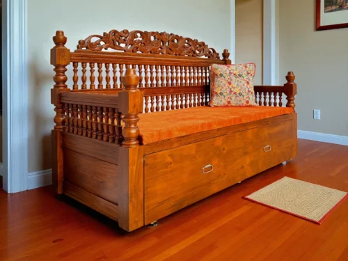 This Teak Wood Sofa Cum Bed is a beautifully crafted piece made exclusively from solid Kerala Teak wood, showcasing exceptional craftsmanship and traditional artistry. The backrest features intricate kadachil work, while the cot is adorned with elegant carvings, including a striking peacock motif. The sides are designed with comfortable hand rests and additional kadachil detailing, offering both style and support. Spacious enough to seat three adults comfortably, the sofa smoothly transforms into a Queen size bed with a strong, stable pull-out mechanism—providing ample space for restful sleep. It comes with a plush cushion set that can be used or removed as preferred, and is available in a variety of fabric color options to suit your interior. A perfect fusion of heritage design and modern utility.