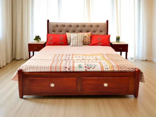 Crafted from rich Kerala Mahogany wood, this King size cot features a luxurious Chesterfield-style upholstered headboard with deep tufting for a timeless look. The design is fully side-covered for a seamless finish, while the front includes two spacious drawers with soft open-close functionality and stylish handles for added elegance. The rounded leg design adds a graceful touch, and fabric color options are available to suit your personal style. A perfect blend of comfort, storage, and craftsmanship—ideal for modern and traditional bedrooms alike.