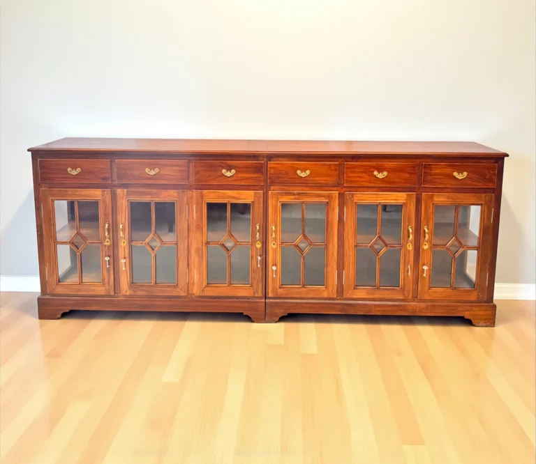 Large teak wood sideboard with six drawers and eight glass-paneled cabinet doors featuring geometric overlays; natural finish with brass handles, ideal for elegant dining or living room storage."