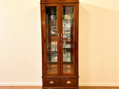 "Tall teak wood crockery shelf with glass doors, glass shelves, and brass shell handles on drawers; natural finish with rounded feet, ideal for elegant dining room display.