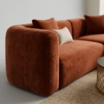 Close-up of rust velvet fabric and rounded arm of L-shaped sofa